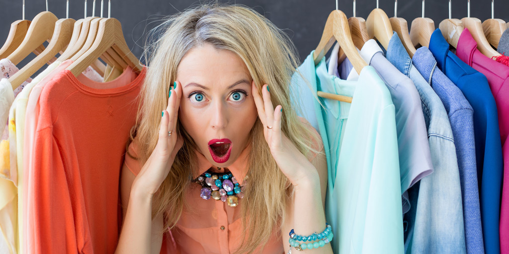 Women standing between hanging clothes in her closet looking stressed.