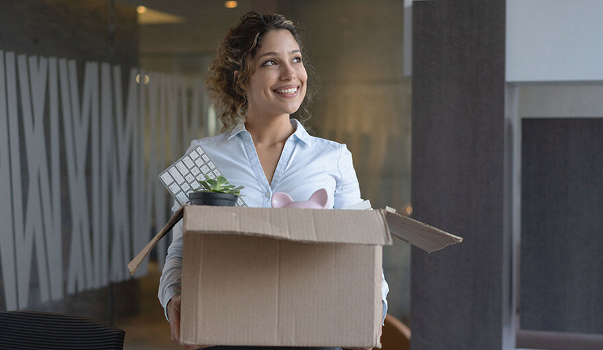 Woman smiling and carrying a box with items used for work