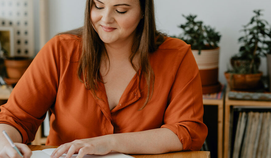 Smiling woman sitting at desk with a pen and paper