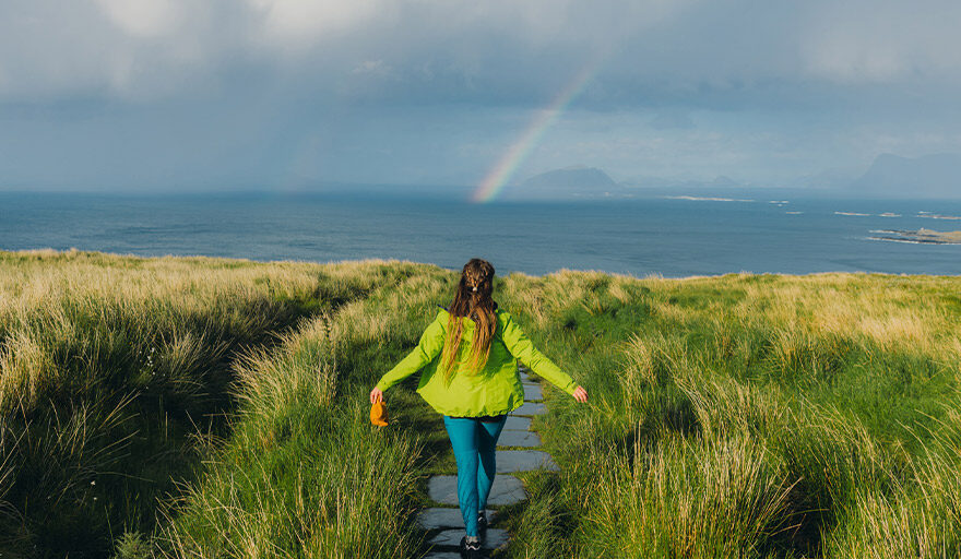 Woman walking in a field towards a the sky with a rainbow