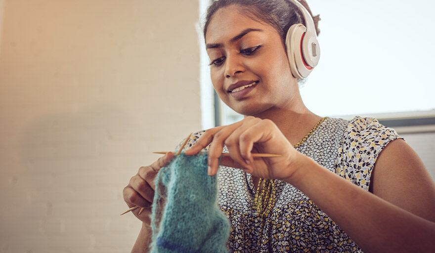 Young woman listening to headphones and knitting