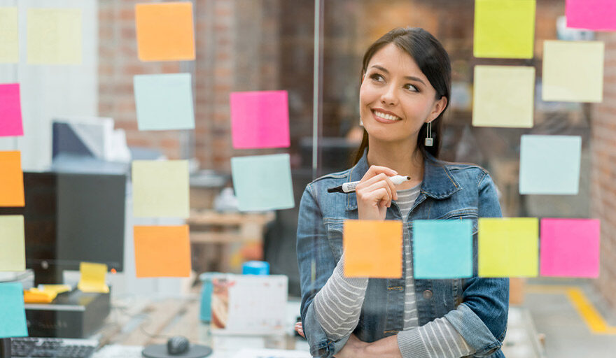 Smiling young woman looking at post-it notes on a wall