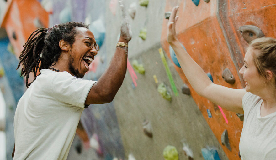 Two people at a rock climbing gym, smiling and high-fiving