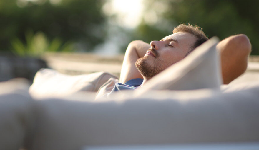 Man lounging on outdoor furniture, looking relaxed.