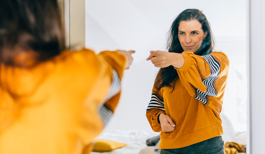 Woman looking in the mirror pointing confidently at herself.