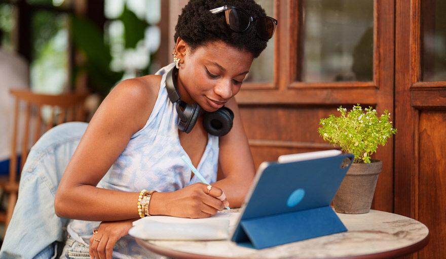Casually dressed woman working on a tablet at a table.