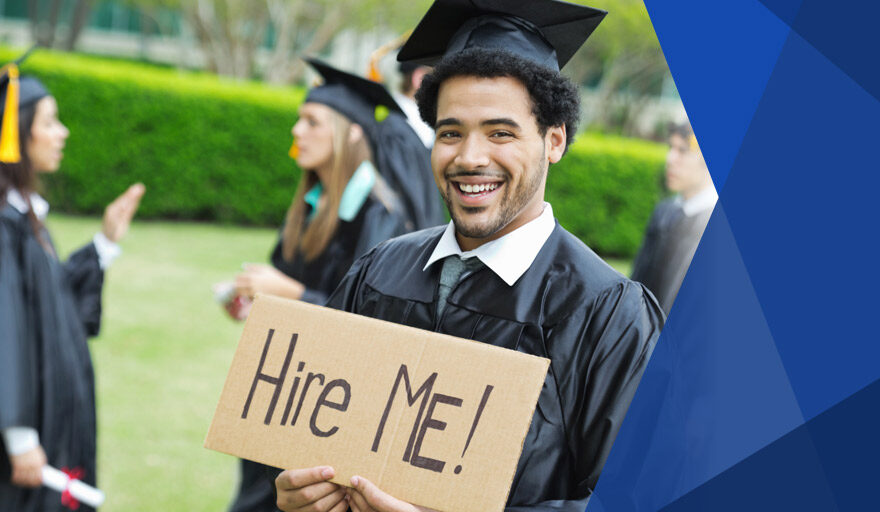 Smiling young man in cap and gown holding a sign that says "Hire Me"