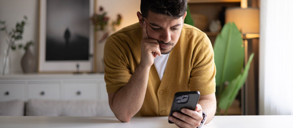 Man leaning forward on a counter while looking at his phone.