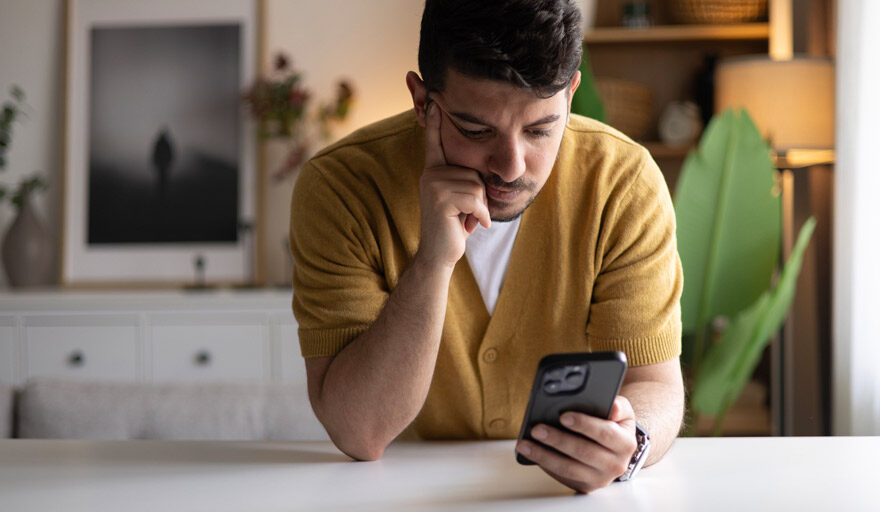 Man leaning forward on a counter while looking at his phone.