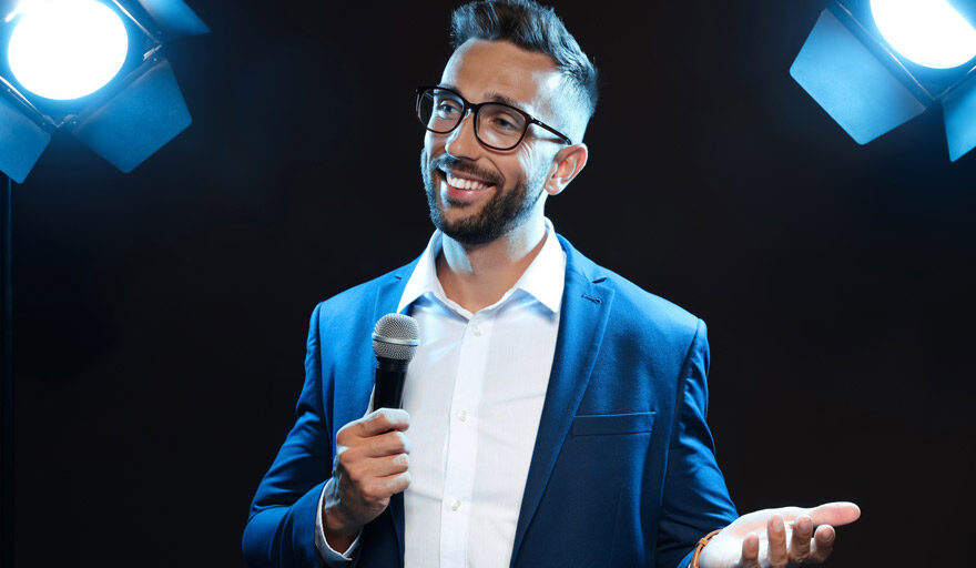Businessman in suit, standing on a stage at an event speaking to a crowd